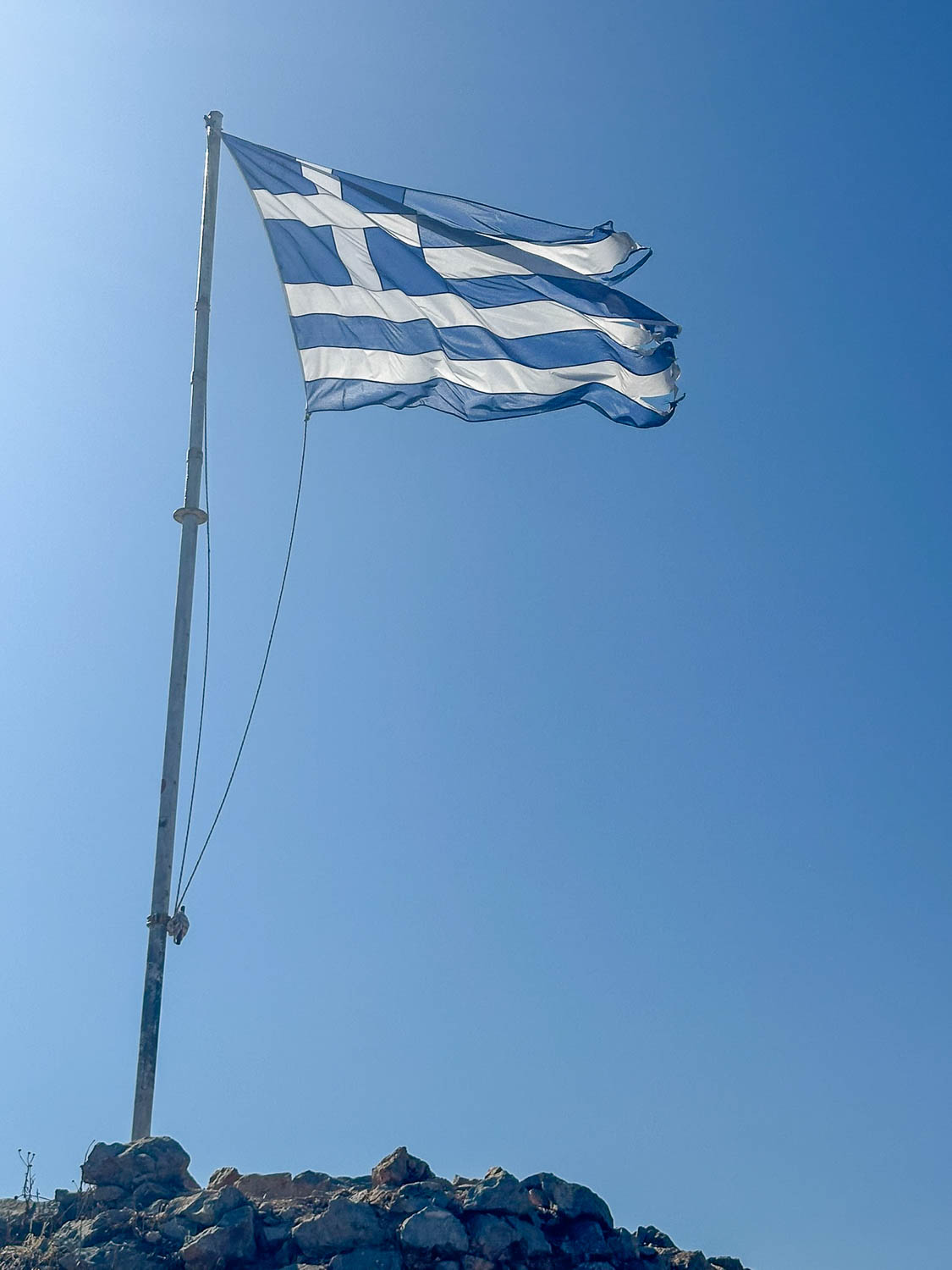 The Greek flag flies proudly atop a rocky outcrop behind Hydra Town Greece